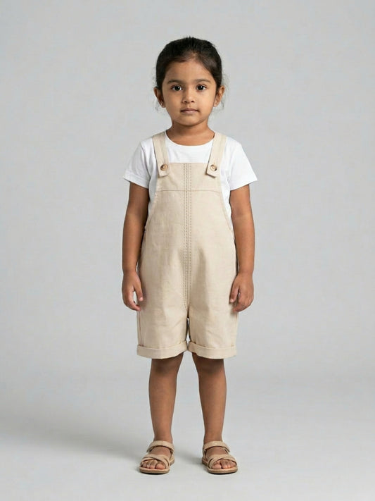 Child wearing beige overalls and a white shirt on a gray background